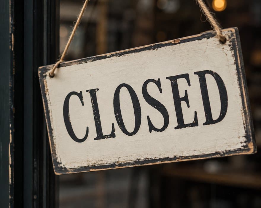 A weathered CLOSED sign hanging in a shop window